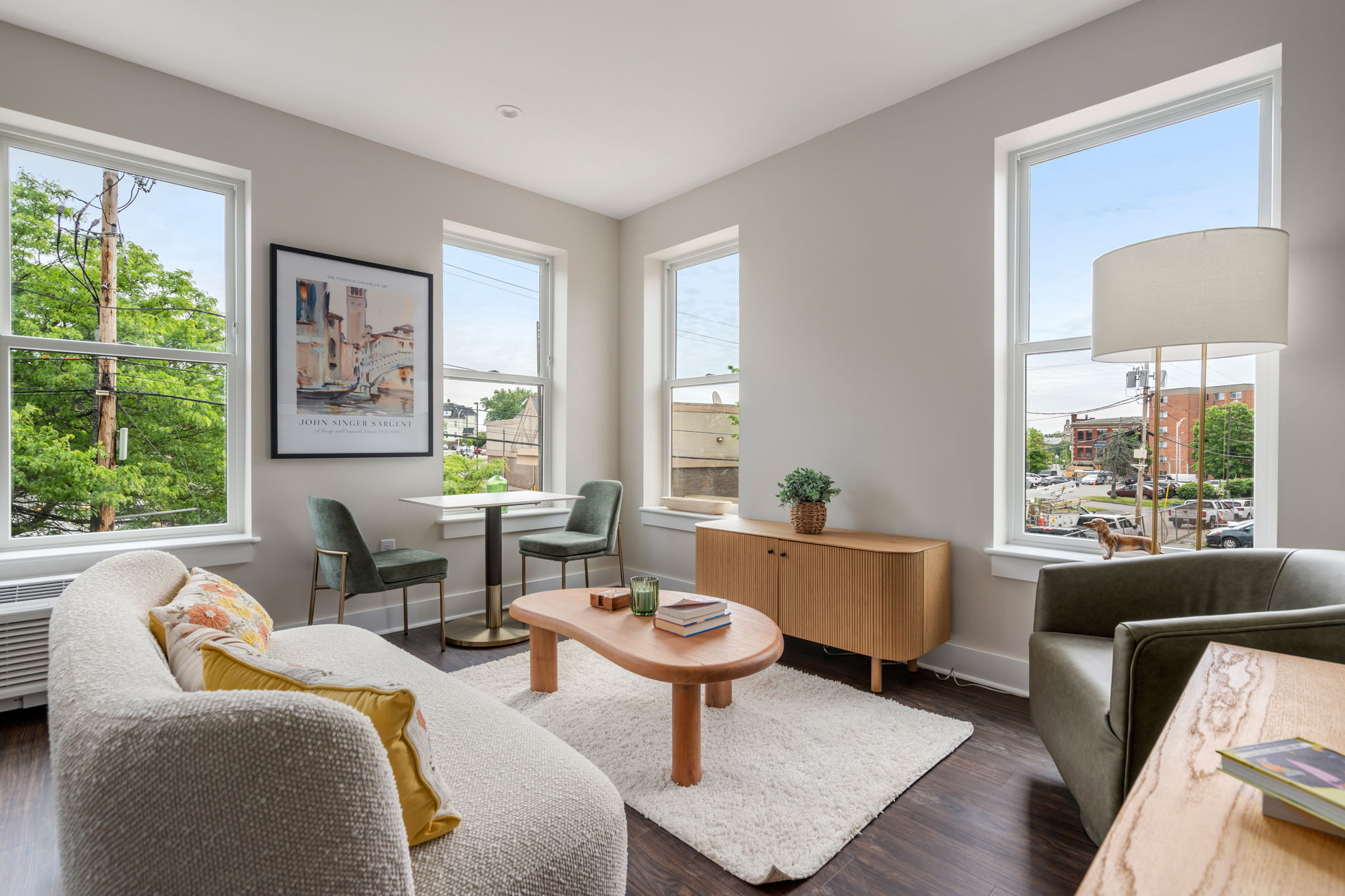 Bright, modern living room with three large windows, light gray walls, a white shag rug, and mint-green chairs around a round coffee table.