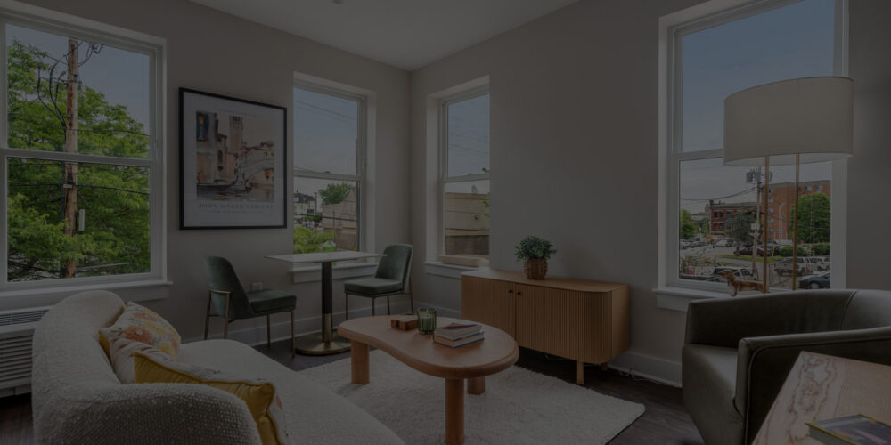 Bright, modern living room with large windows, gray walls, and a round wooden coffee table between a sofa and chairs.