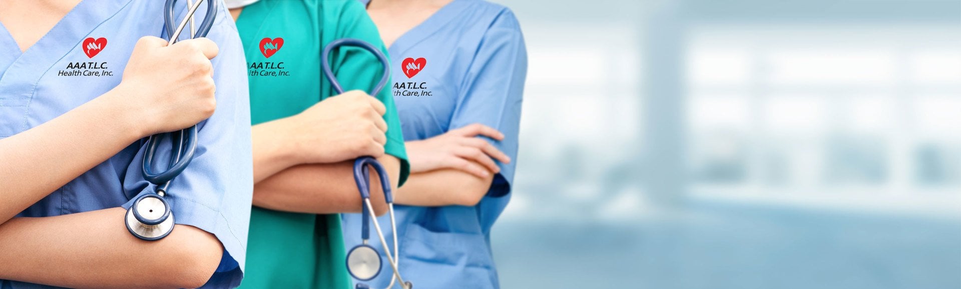 Three healthcare professionals in scrubs with stethoscopes, arms crossed, with visible logos on their uniforms in a hospital setting as a backdrop.